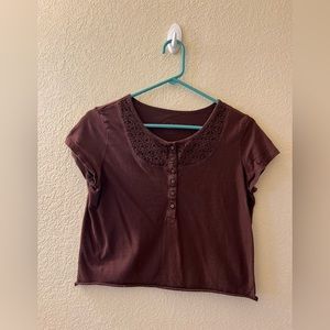 Brown shirt with brown buttons down the center. Crochet detailing at the top.